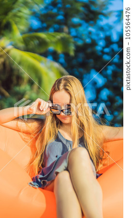 Summer lifestyle portrait of pretty girl sitting on the orange inflatable sofa on the beach of tropical island. Relaxing and enjoying life on air bed VERTICAL FORMAT for Instagram mobile story or Summer lifestyle portrait of pretty girl sitting on the orange inflatable sofa on the beach of tropical island. Relaxing and enjoying life on air bed VERTICAL FORMAT for Instagram mobile story or 105564476