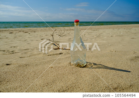 White glass bottle on the sandy beach in the sun, sea or ocean waste concept. Baltic Sea Latvia White glass bottle on the sandy beach in the sun, sea or ocean waste concept. Baltic Sea Latvia 105564494