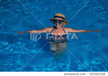 Portrait of an elderly woman in a hat and blue sunglasses swims in the pool.  105565286