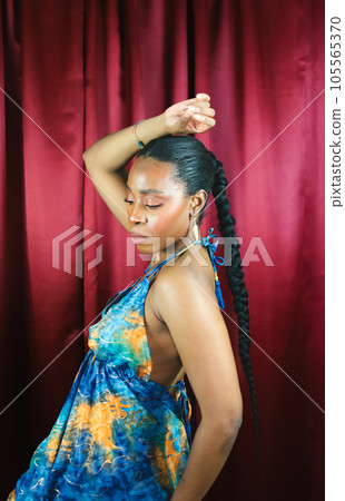 African Woman ethnicity with blue dress dancing and smiling in red background 105565370