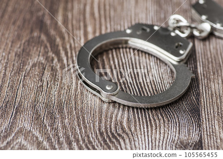 The metal handcuffs on wooden background. Handcuff or shackle. Police handcuffs The metal handcuffs on wooden background. Handcuff or shackle. Police handcuffs 105565455