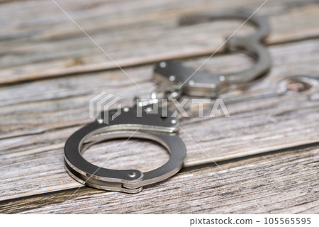 The metal handcuffs on wooden background. Handcuff or shackle. Police handcuffs The metal handcuffs on wooden background. Handcuff or shackle. Police handcuffs 105565595