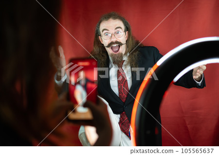 Funny Caucasian Man posing at photography studio while being shot by cell phone Funny Caucasian Man posing at photography studio while being shot by cell phone 105565637