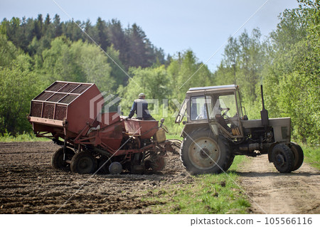 Potato planter is hitched to wheeled agricultural tractor in farmer field. Potato planter is hitched to wheeled agricultural tractor in farmer field. 105566116