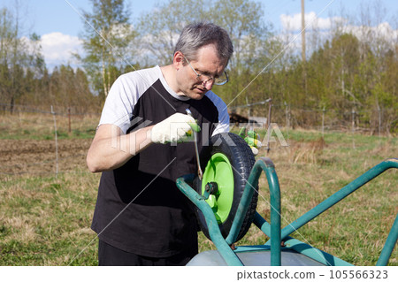 Installing new pneumatic wheel on garden cart, farmer repairs garden equipment. Installing new pneumatic wheel on garden cart, farmer repairs garden equipment. 105566323