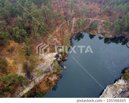 Picturesque aerial view of landscape with emerald lake and rocks in the middle of a coniferous autumn forest in Korostyshiv granite quarry, Zhytomyr district, northern Ukraine. Zhytomyr canyon 105566885