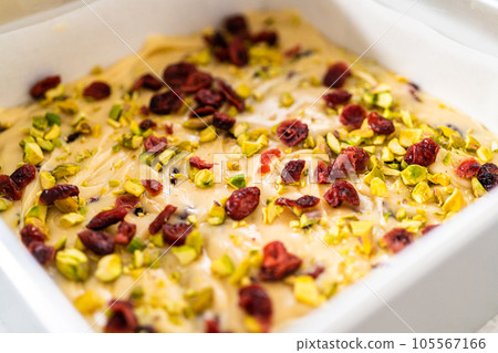 Removing cranberry pistachio fudge from a square cheesecake pan lined with parchment. 105567166