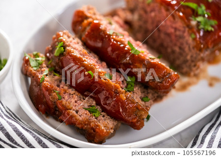 Slicing classic meatloaf with a sweet glaze on a white serving plate Slicing classic meatloaf with a sweet glaze on a white serving plate 105567196