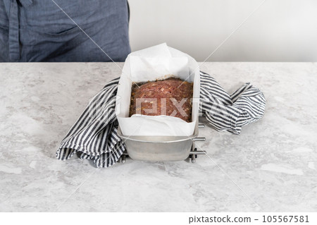 Glazing classic meatloaf with sweet glaze in a loaf pan lined with parchment paper. Glazing classic meatloaf with sweet glaze in a loaf pan lined with parchment paper. 105567581