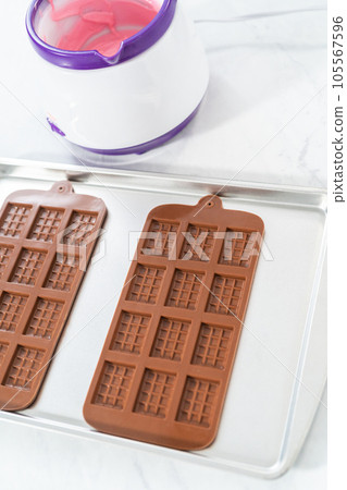 Filling silicone chocolate mold with melted chocolate to make mini pink chocolates. 105567596