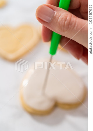 Decorating heart-shaped sugar cookies with pink and white royal icing for Valentine's Day. 105567632
