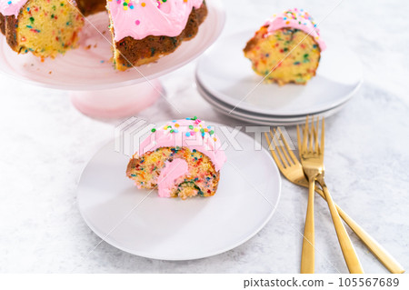 Sliced funfettti bundt cake with pink buttercream frosting on top and buttercream filling inside. 105567689