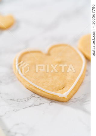Decorating heart-shaped sugar cookies with pink and white royal icing for Valentine's Day. 105567796