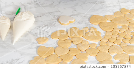 Decorating heart-shaped sugar cookies with pink and white royal icing for Valentine's Day. Decorating heart-shaped sugar cookies with pink and white royal icing for Valentine's Day. 105567874