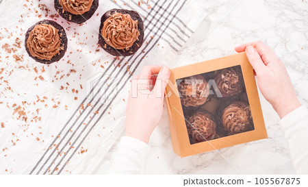 Flat lay. Step by step. Packaging chocolate cupcakes with chocolate ganache frosting into a paper cupcake box. 105567875