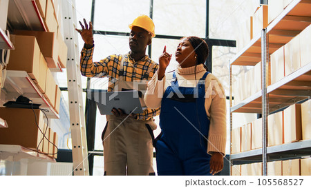 African american employees using laptop in storage room, man and woman checking merchandise and warehouse stock in depot. Team of workers analyzing logistics on pc. Handheld shot. 105568527