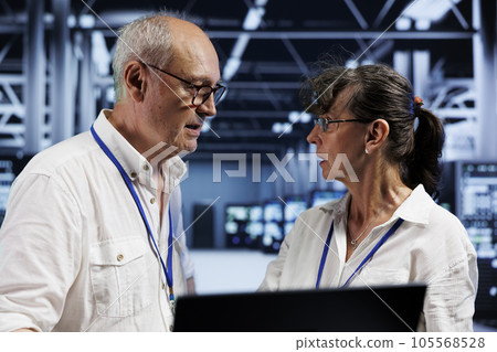 Elderly coworkers preventing strain on data center machines caused by AI applications driving up power usage. Teamworking colleagues maintenancing server clusters doing intense computations 105568528