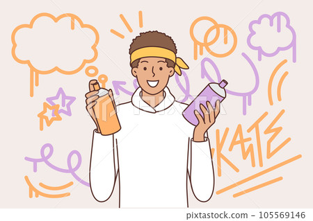 Teenager guy draws graffiti on wall, holds spray can of paint and smiling looks at camera Teenager guy draws graffiti on wall, holds spray can of paint and smiling looks at camera 105569146