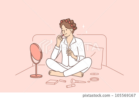 Woman does makeup while sitting in bed early in morning and paints lips while looking in mirror Woman does makeup while sitting in bed early in morning and paints lips while looking in mirror 105569167