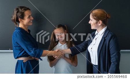 The teacher shakes hands with the mother of the schoolgirl standing at the blackboard. The teacher shakes hands with the mother of the schoolgirl standing at the blackboard. 105569468