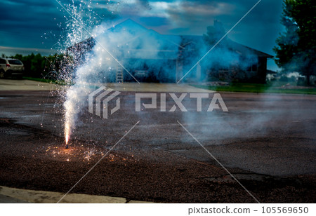 A fountain of sparks, flames, and smoke emitting from a fountain fireworks being set off in a residential neighborhood. A fountain of sparks, flames, and smoke emitting from a fountain fireworks being set off in a residential neighborhood. 105569650