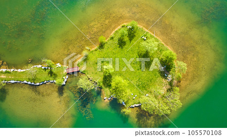 Aerial over teal green pond with small island and land bridge leading to red walking bridge Aerial over teal green pond with small island and land bridge leading to red walking bridge 105570108