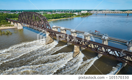 Truss arch bridge over large dam blue river water and white water rapids aerial of distant shore 105570330