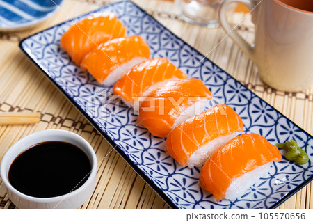 Blue rectangular ceramic plate of delicious salmon nigiri with soy souse on bamboo mat. 105570656