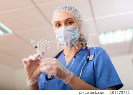 Female nurse in mask holding syringe for injection Female nurse in mask holding syringe for injection 105570751