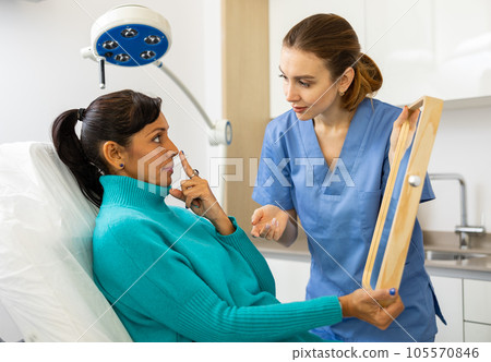 Latin woman holding mirror during cosmetologist's consultation 105570846