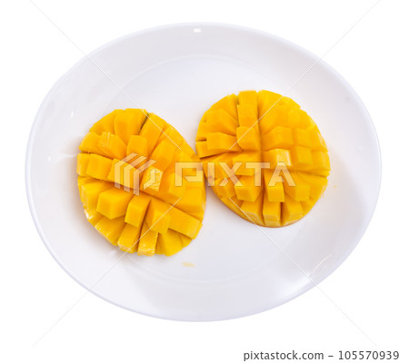 Two halves of ripe yellow mango cut into cubes lie on white round plate 105570939