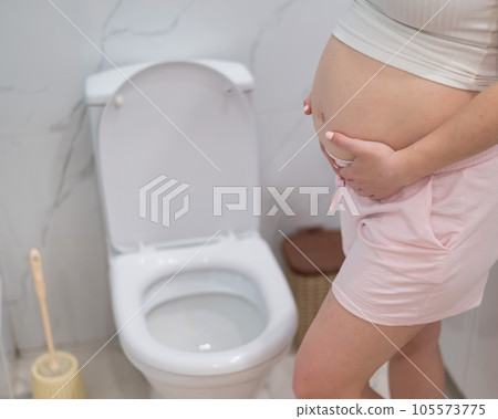 Pregnant woman holding her belly in the toilet. incontinence during pregnancy.  105573775