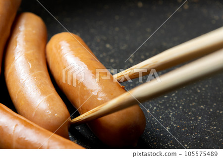 A cooking scene in which the wiener sausage is cut in and baked in a frying pan. 105575489