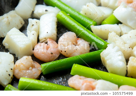 A cooking scene where seafood (squid and shrimp) and garlic sprouts are fried in a frying pan. A cooking scene where seafood (squid and shrimp) and garlic sprouts are fried in a frying pan. 105575499