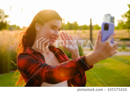 Portrait of red haired wearing plaid shirt young blogger says hello to her followers and records story using mobile phone Portrait of red haired wearing plaid shirt young blogger says hello to her followers and records story using mobile phone 105575830