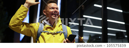 Happy man with smartphone smiles and greets friends with raised hand outdoors. Happy man with smartphone smiles and greets friends with raised hand outdoors. 105575839