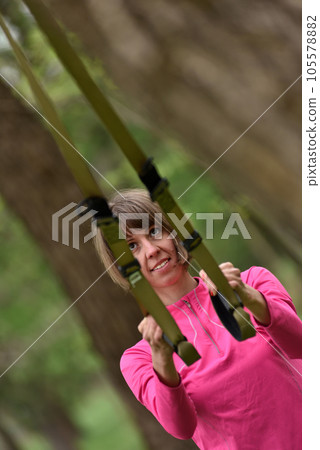Woman doing arms biceps curl training with trx fitness straps 105578882