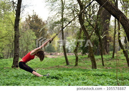 Young attractive woman does body stretching with trx fitness straps Young attractive woman does body stretching with trx fitness straps 105578887