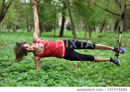 Beautiful young woman doing TRX exercise with suspension trainer sling in the outdoors Beautiful young woman doing TRX exercise with suspension trainer sling in the outdoors 105578888