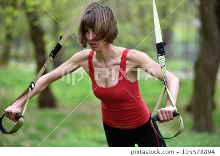 Young woman does suspension training with fitness straps in the outdoors Young woman does suspension training with fitness straps in the outdoors 105578894