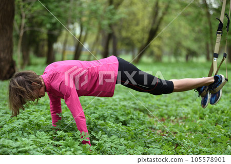 Beautiful young woman doing TRX exercise with suspension trainer sling in the outdoors Beautiful young woman doing TRX exercise with suspension trainer sling in the outdoors 105578901