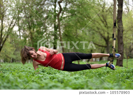 Beautiful young woman doing TRX exercise with suspension trainer sling in the outdoors Beautiful young woman doing TRX exercise with suspension trainer sling in the outdoors 105578903