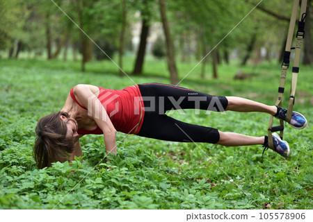 Beautiful young woman doing TRX exercise with suspension trainer sling in the outdoors Beautiful young woman doing TRX exercise with suspension trainer sling in the outdoors 105578906