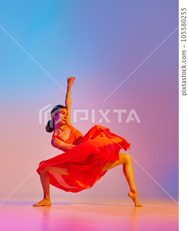 Classic and modern. Elegant young woman dancing contemp in dress against gradient multicolor background in neon light 105580255