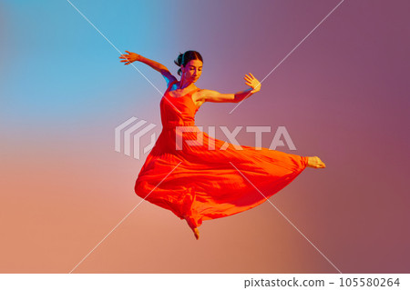 Dynamic image of young talented, artist woman in elegant red dress dancing against gradient multicolored background in neon light 105580264