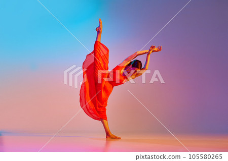 Dynamic image of young talented, artist woman in elegant red dress dancing against gradient multicolored background in neon light 105580265