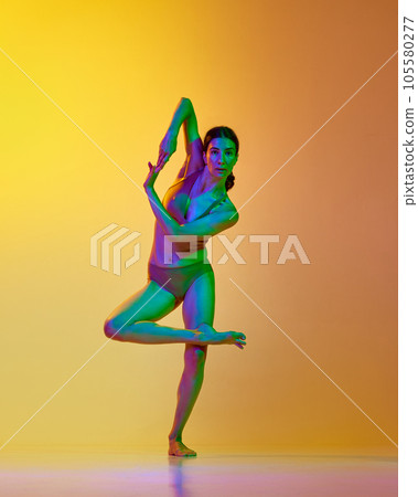 Full-length image of young woman, professional dancer in motion, dancing in underwear against gradient yellow orange background in neon light Full-length image of young woman, professional dancer in motion, dancing in underwear against gradient yellow orange background in neon light 105580277