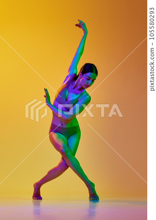 Tender young woman in underwear dancing contemp dance against gradient yellow orange background in neon light Tender young woman in underwear dancing contemp dance against gradient yellow orange background in neon light 105580293