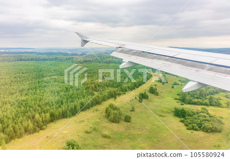 View of airplane wing, blue skies and green land during landing. Airplane window view. 105580924