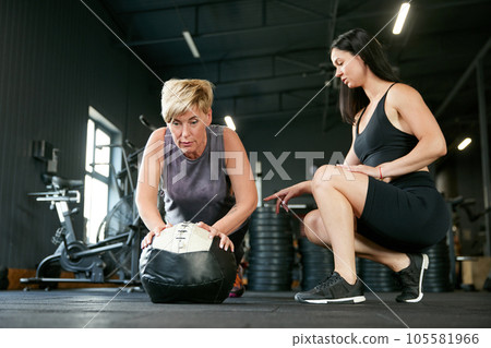 Sportive mature woman training in gym with female fitness trainer, doing push ups exercises. Strength, endurance 105581966